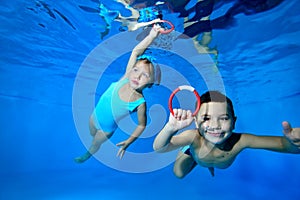 Happy little children, a boy and a girl, play and have fun under the water in the children`s pool. They swim with their