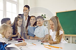 Happy little children learning draw in elementary school stand in classroom with woman teacher