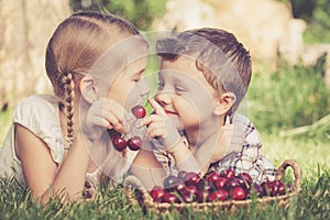 Happy little children lying near the tree with a basket of cherries at the day time.