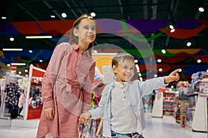 Happy little children walk among display cases with toys in store