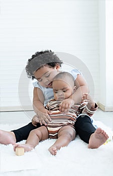 Happy Little cute African chubby kid girl hugging her newborn baby sister in arms while sitting playing together on floor at home