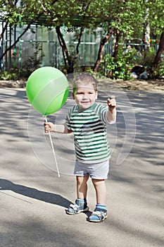 Happy little cute boy holds green balloon and smiles