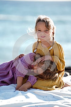 Happy little cute girls enjoying sunny day at the beach, hugging and smiling to the camera. Family summer vacation. Sister`s love
