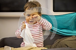 Happy little cute toddler wake up in special baby bassinet of the plane, smile, rubs eyes and holds wet hot towel after