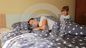 Happy little daughter wakes up her sleeping father early in the morning in bed at home. morning concept