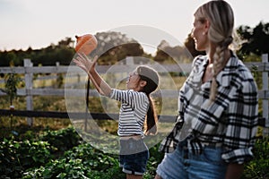 Happy little farmer girl throwing pumpkin with mother outdoors at garden.