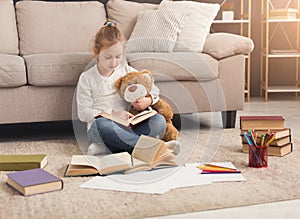 Happy little female child hugging her teddy bear and reading