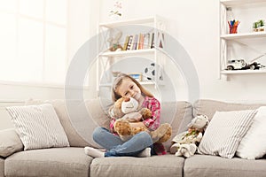 Happy little female child hugging her teddy bear on sofa at home