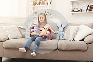 Happy little female child hugging her toy rabbits on sofa at home