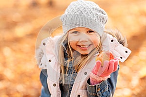 Happy little girl with apple at autumn park