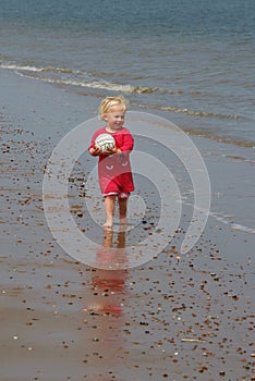 Happy little girl on the beach with a ball