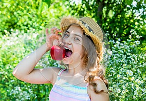 Happy little girl bite ripe red apple fruit in summer garden on sunny outdoors, vitamin