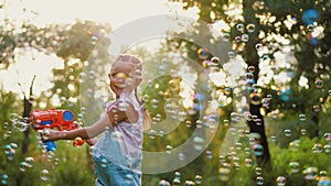 Happy little girl blowing soap bubbles, playing in park outdoors with toy gun