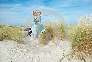 Happy little girl in blue dress jumping on beach at sunny day