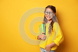 Happy little girl with books on yellow background