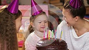 Happy little girl celebrates her birthday with her family, her mother and teenager sister helps blow out the candles
