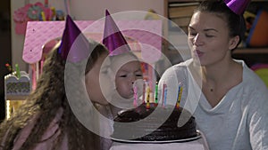 Happy little girl celebrates her birthday with her family, her mother and teenager sister helps blow out the candles