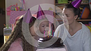 Happy little girl celebrates her birthday with her family, her mother and teenager sister helps blow out the candles