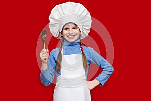 Happy little girl in chef uniform holds spoon