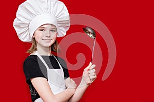 Happy little girl in chef uniform holds spoon isolated on red. Kid chef. Cooking Concept