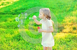 Happy little girl child blowing soap bubbles in summer