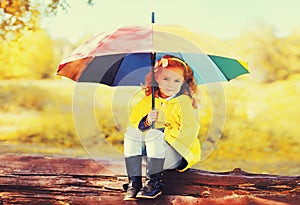 Happy little girl child with colorful umbrella in sunny autumn park