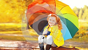 Happy little girl child with colorful umbrella in sunny autumn park