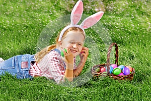 Happy little girl child on the day of Easter is looking for colorful eggs in a basket and folds