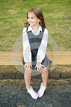 Happy little girl child in formal school uniform sit on park bench, schoolgirl