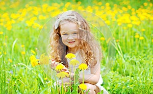 Happy little girl child on grass with yellow dandelion flowers in summer