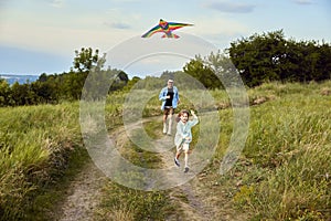 Happy little girl, child running with kite on trail in field. Spending time with parents outdoors on warm summer day