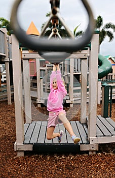 Happy Little Girl Child Swinging on Monkey Bar Rings at Playground