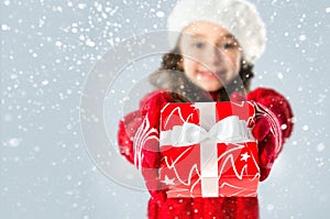 Happy little girl with Christmas gift on snow background
