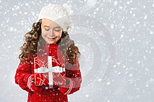 Happy little girl with Christmas gift on snow background