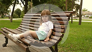 Happy little girl climbs on a big park bench. cheerful little child stands on a park bench. concept of happy childhood