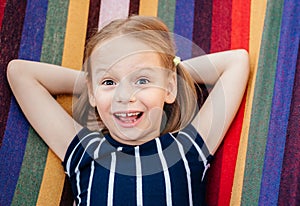 Happy little girl with crooked baby teeth in the colorful hammock summer background, summer holiday outdor activities