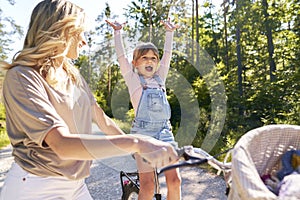 Happy little girl cycling with her mother in the forest