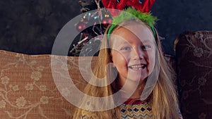 Happy little girl in deer horns laughs looks into camera at home 4K portrait. Smiling toothless child New Year Christmas