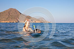 Happy little girl with diving glasses on back of woman snorkeling in the water of a beach in Andalusia