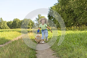 Happy little girl with dog running in park, summer field. child playing with puppy outdoors.