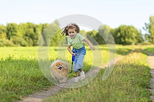 Happy little girl with dog running in park, summer field. child playing with puppy outdoors.