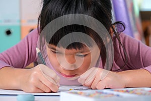 Happy little girl drawing with colored pencils on paper sitting at table in her room at home. Creativity and development of fine