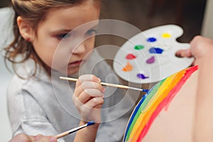 Happy little girl drawing rainbow on pregnant belly her mother. Baby birth expecting time and belly painting