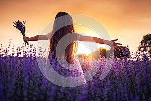 Happy little girl with dress enjoying lavender field with bouquet of flowers