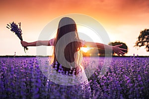 Happy little girl with dress enjoying lavender field with bouquet of flowers