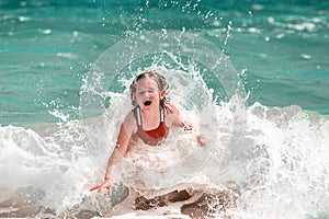 Happy little girl enjoying sea waves. Child playing in the sea. Kid in swimming suit having fun on the sand beach
