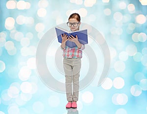 Happy little girl in eyeglasses reading book