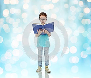 Happy little girl in eyeglasses reading book