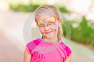 Happy little girl with face art paint in the park.