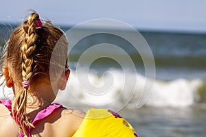 Happy little girl with floaties floaties preparing to swim in the ocean